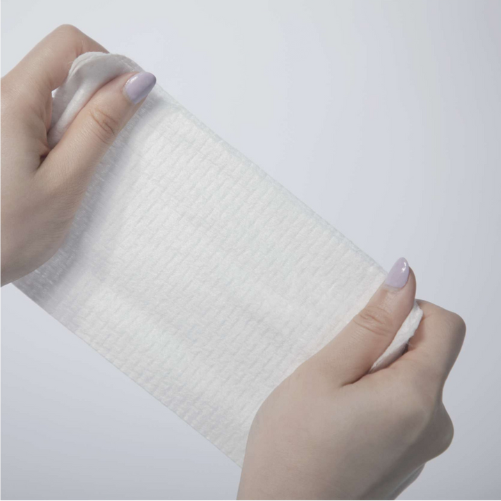 Close-up of hands holding a Dermalume disposable facial wipe, showing its soft textured surface.