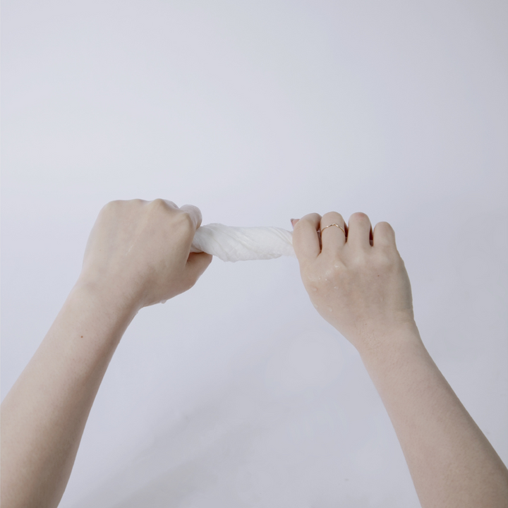 Hands wringing out a Dermalume disposable facial wipe to demonstrate its durability and absorbency.